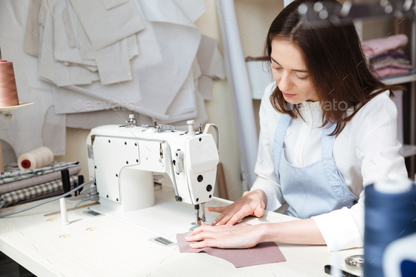 Professional dressmaker woman sews clothes on sewing machine at