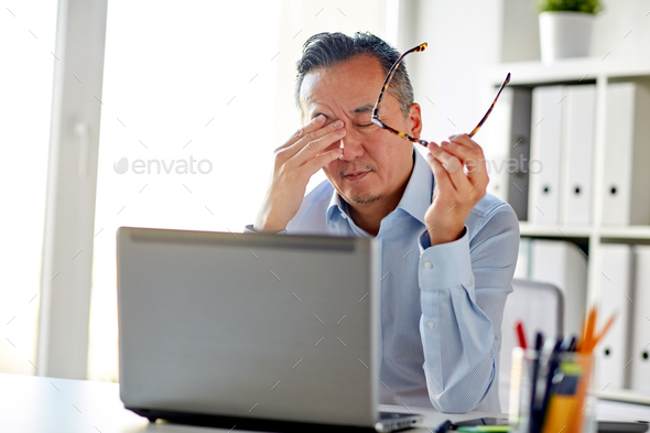 tired businessman with glasses at laptop in office - Stock Photo - Images