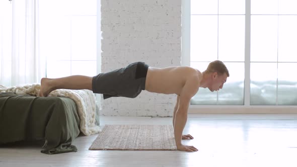 Sporty Young Man Is Doing Push Ups Exercise with Legs on Bed at Home Side View
