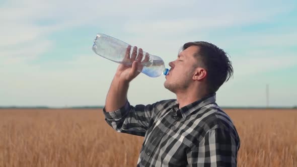 A Farmer Stands in a Field of Wheat and Slowly Drinks Water From a Bottle