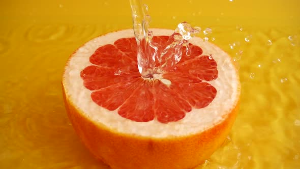 Half of a grapefruit in a jet of water on an orange background. Slow motion. alt