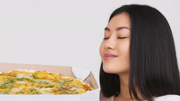 Asian Woman Smelling Pizza Holding Box Near Face White Background alt