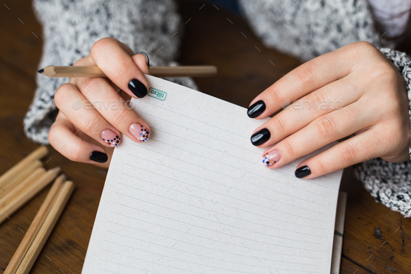 A woman with a beautiful manicure draws in a notebook Stock Photo by ollinka