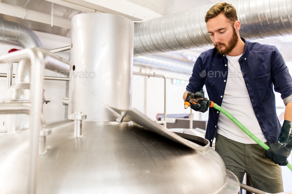 man with hose working at craft beer brewery kettle - Stock Photo - Images