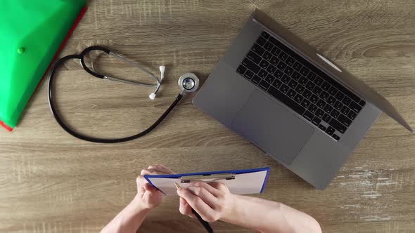 The Doctor is Writing the Symptoms of Patient at the Wooden Table