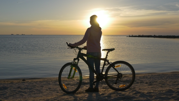 Cyclist Standing Near Water and Watching Sunset