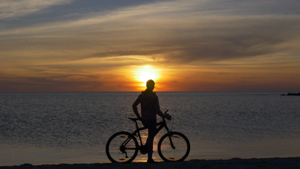 Female Cyclist Relaxing on the Beach at Sunset
