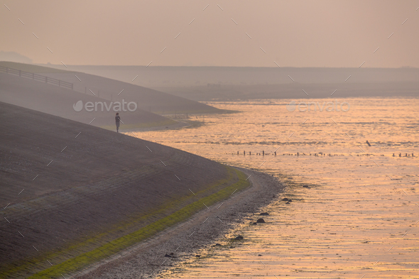 Person watching sunset from Sea dike in orange haze