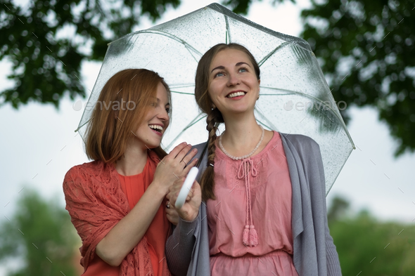 Two women walking park in rain and talk. Friendship and people communication.