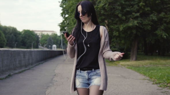 Young Hipster Woman Walking with Smartphone in Park and Dancing