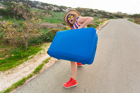 Young woman with blue suitcase making funny faces outdoors