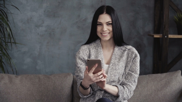 Young Woman Using Smartphone and Smiling at Home