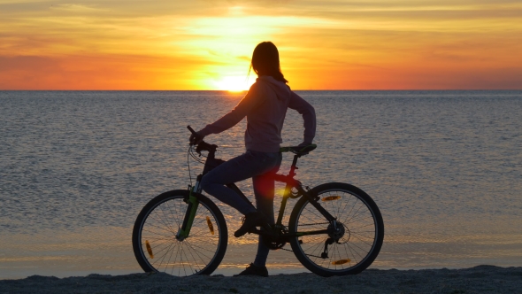 Woman on Bicycle Looking at Sunset Over the Sea