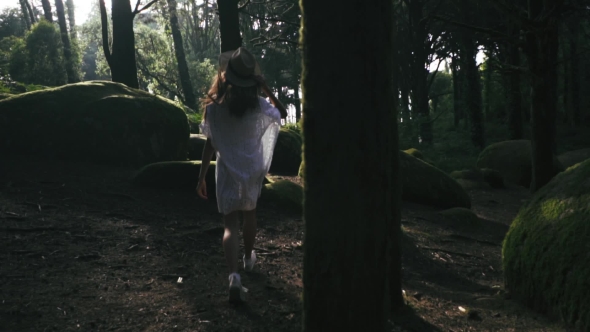 Young Sexy Woman in White Dress with Straw Hat Is Running in the Green Forest Jumping and Touching
