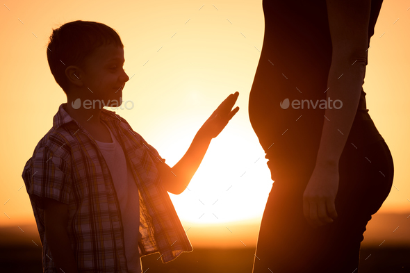 Mother and son walking on the field at the sunset time.