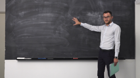 Young Teacher Man Explains Something at Clean Blackboard