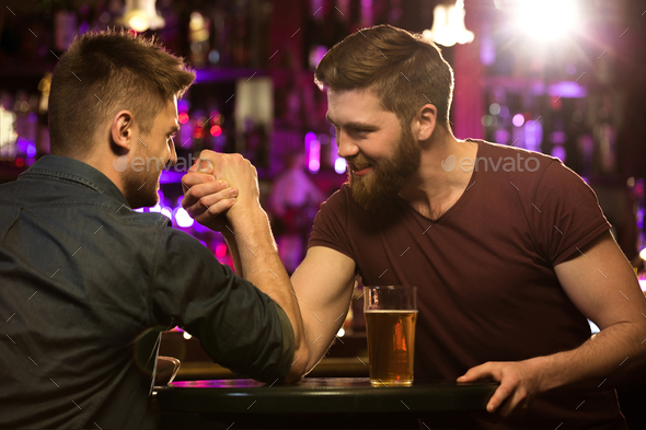 happy male friends drinking draft beer and arm wrestling