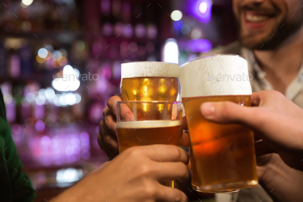 Young men toasting with beer while sitting in pub together