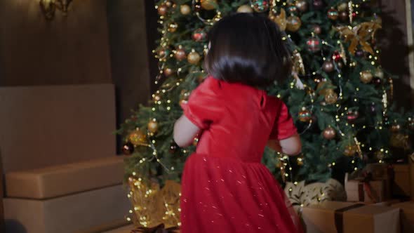 Korean Girl Child in a Red Dress Stands at the Christmas Tree in New Year alt