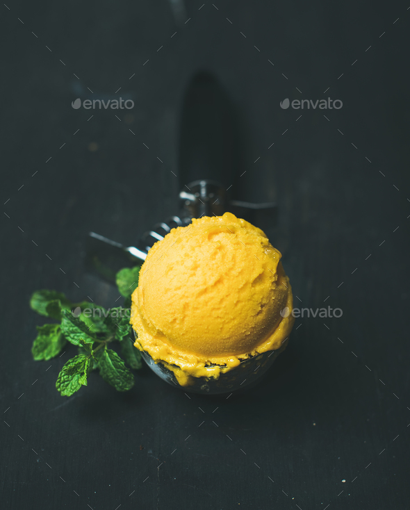 Mango sorbet ice cream scoop in scooper over black background - Stock Photo - Images