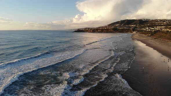 A drone flies high above crashing waves at the beach with a beautiful sky backdrop. alt