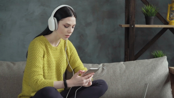 Beautiful Woman in Headphones Using Smartphone at Home