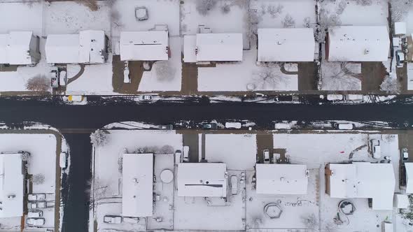 Slowly flying over snow covered houses looking down at street alt