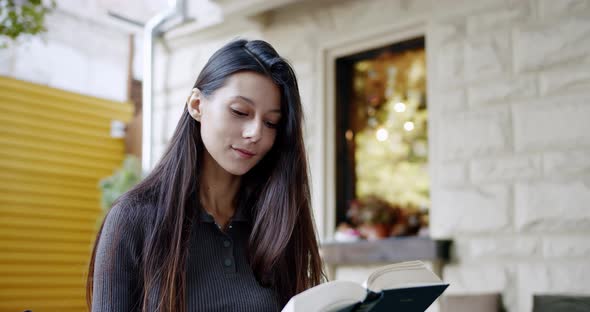 Smiling Young Woman is Reading Interesting Book Outdoor Leafing Through a Book alt