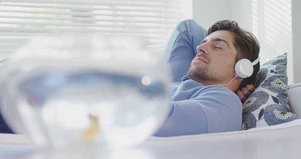 Gold fish bowl and man lying on sofa wearing headphones listing music 4K 4k alt