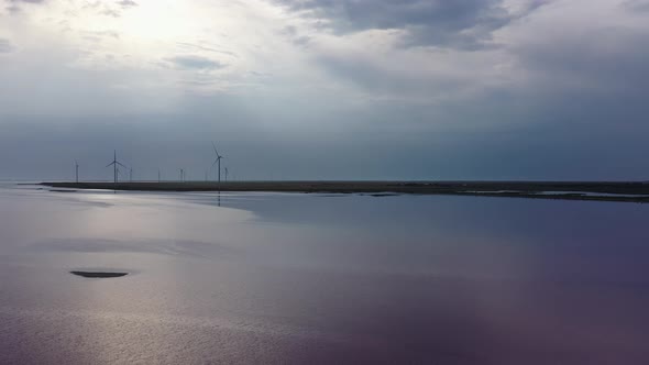 A wind farm on the shores of a pink lake. Evening time. Aerial view.