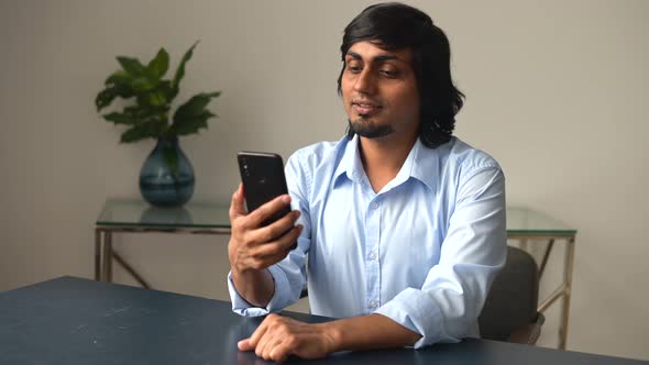 Contemporary Cheerful Indian Colleague Holding Smartphone and Waving Hand