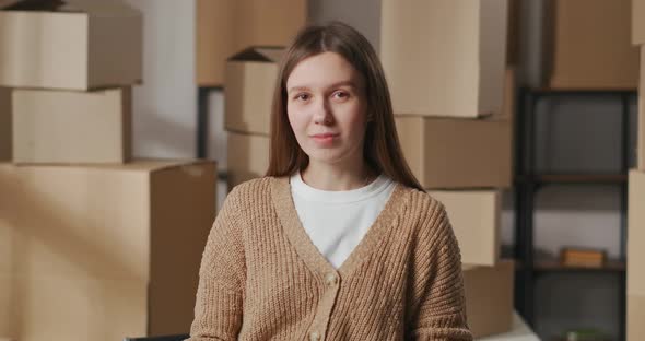 Beginner Entrepreneur Woman Is Standing in Her Warehouse with Handmade Goods Against Cardboard Boxes alt