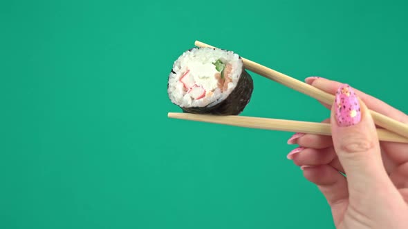 Female Hands Hold Japanese Chopsticks with Sushi Rolls on Green Background alt