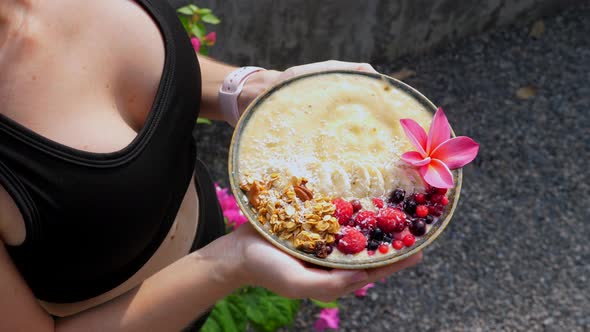 Hands Holding Banana Fruit Smoothie Bowl Served with Berries and Granola alt