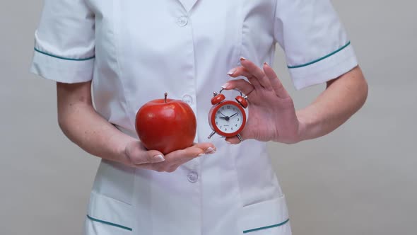 Nutritionist Doctor Healthy Lifestyle Concept - Holding Organic Red Apple and Alarm Clock alt