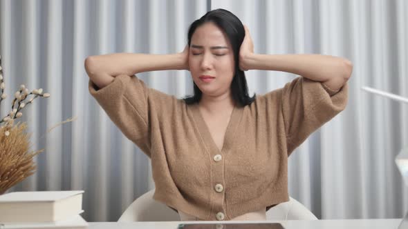 Close-up of a stressed Asian woman rubbing her temples due to a headache.