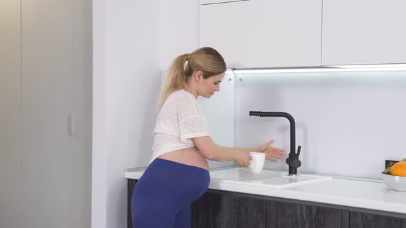 Pregnant Woman at Home Pours Water Into a Glass and Drinks It