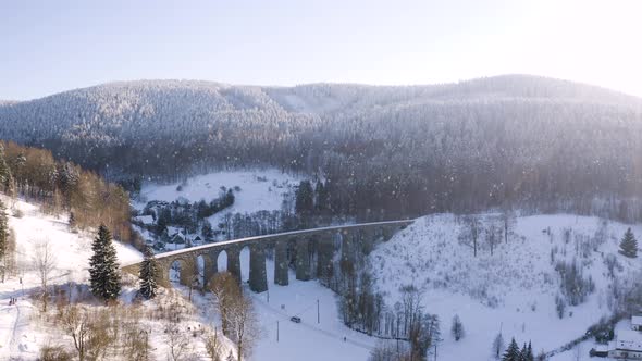 Winter countryside with a stone train viaduct in falling snow,sunny. alt