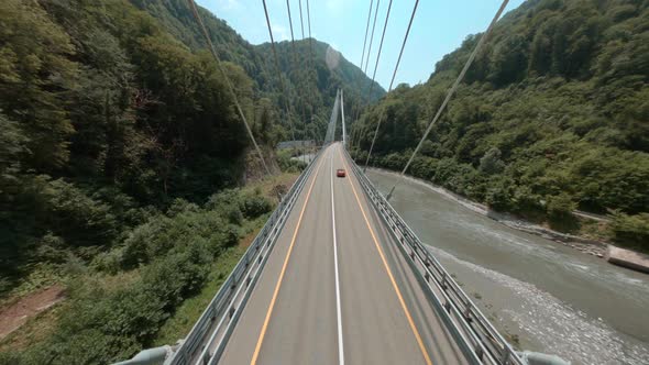 Red Car Drives Along Cable-stayed Bridge Over Mountain River alt