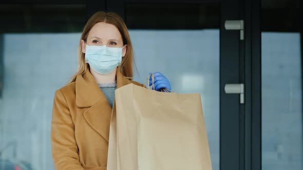 Woman in Gloves and Mask with Bags of Groceries on the Background of Entering the Grocery Store alt