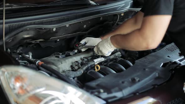 The Hands of an Auto Mechanic Use a Socket Wrench To Unscrew Parts Under the Hood of a Car