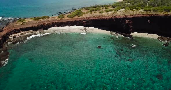 Drone shots of a cliff side beach with blue waters and no one around. alt