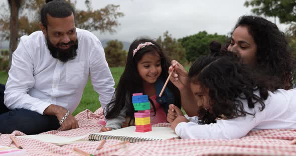 Indian parents having fun at city park playing with wood toys with their children alt