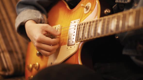 The girl plays the guitar on the couch. A woman creates music indoors. The artist performs on the ba