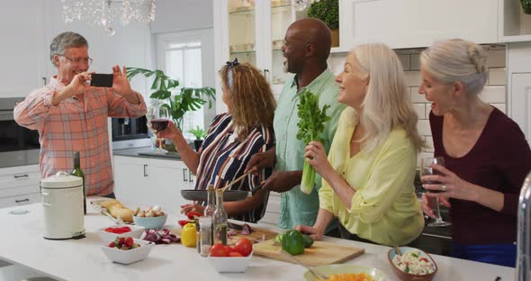 Animation of happy diverse female and male senior friends preparing meal, taking photo alt
