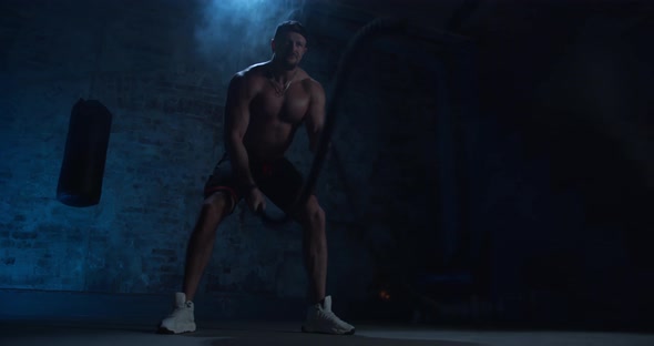 Fitness Muscular Man Exercising with Battle Rope Abandoned Warehouse