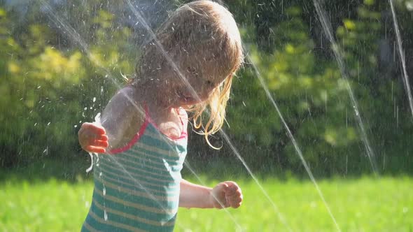 The Cute Little Girl in Swimsuits is Playing with a Water Sprinkler on ...