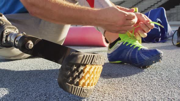 Low section of caucasian disabled male athlete sitting, tying shoe alt