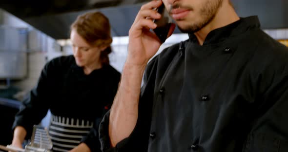 Chef looking at clipboard while talking on mobile phone 4k alt