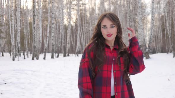 Young Woman with Wavy Hair Standing and Touching Face in Winter Forest